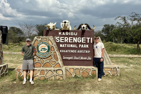 Two teenage boys stand next to Serengeti National Park entrance gate